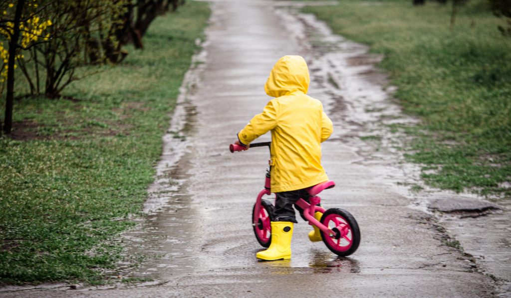 small child with a raincoat riding a small bmx