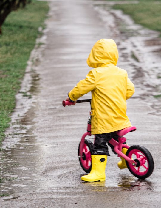 small child with a raincoat riding a small bmx