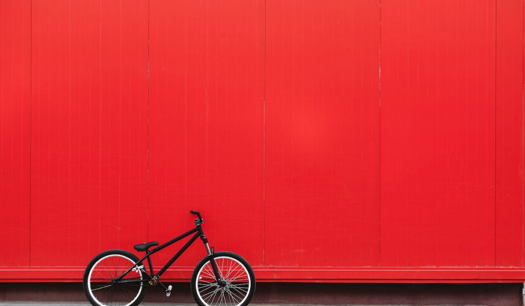 Black bicycle stands nearby red wall, bmx