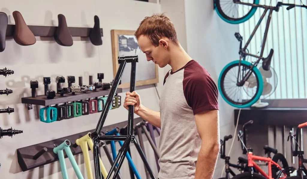 Teenage BMX rider holding a bicycle frame and choosing parts for his BMX in a shop