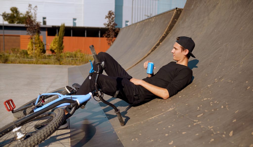 Young male bmx biker resting in ramp in skatepark with his BMX