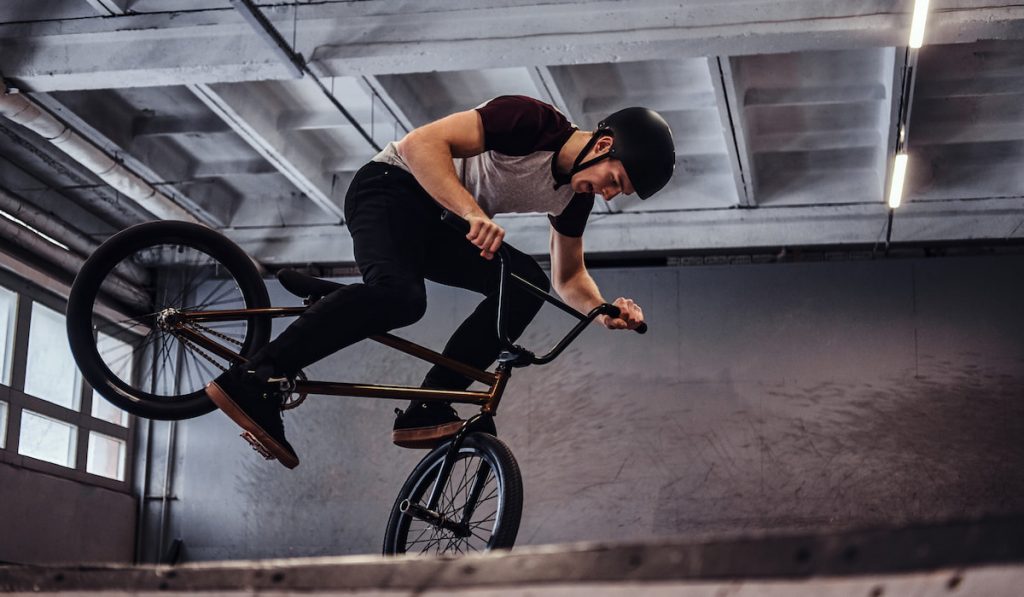 man wearing helpmet with BMX performing tricks in skatepark indoors